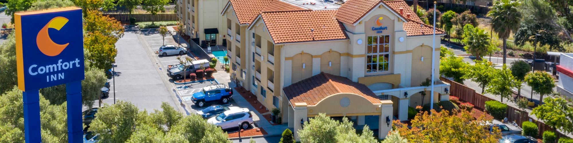 Aerial view of a Comfort Inn hotel with a large parking lot, surrounded by greenery and hills in the background.