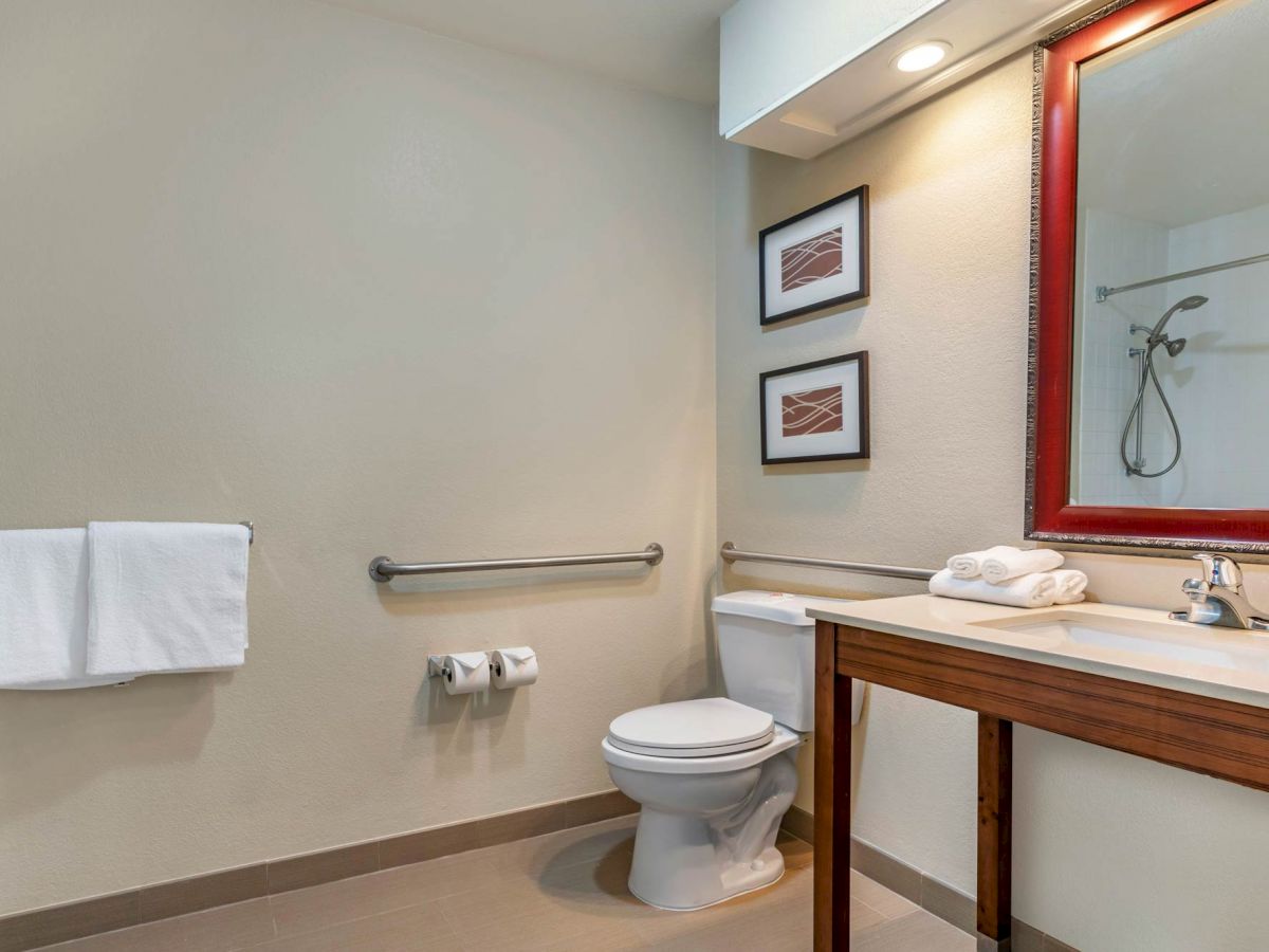 A clean bathroom with a toilet, sink, mirror, artworks on the wall, hand towel, and two toilet paper rolls.