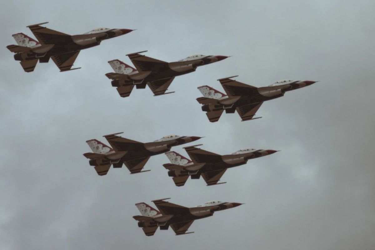 The image shows six fighter jets flying in formation against a cloudy sky.