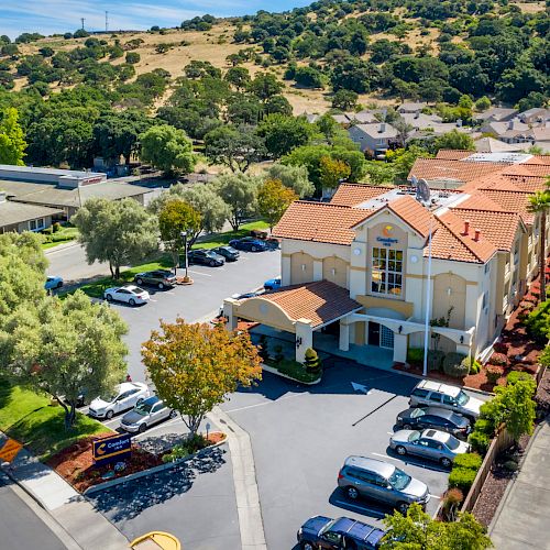 An aerial view of a Comfort Inn hotel, surrounded by trees, a parking lot with several cars, and a scenic hillside in the background.