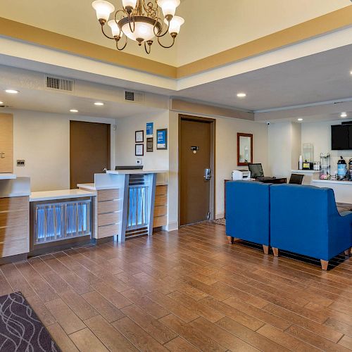 The image shows a hotel reception area with check-in counters and a seating area with blue chairs. There is a chandelier on the ceiling.