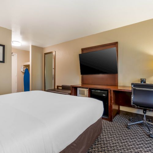 A neatly arranged hotel room with a bed, desk, chair, flat-screen TV, lamp, wall art, and an iron in the open closet.