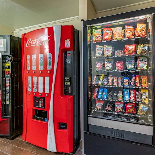 Three vending machines, one with beverages, one with various snacks, and another with Coca-Cola drinks, are placed side by side in a room.