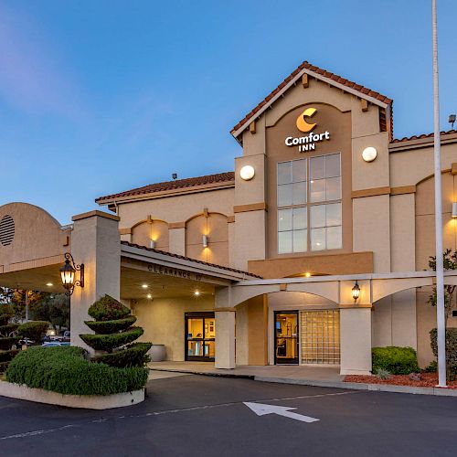 It's an image of the exterior of a Comfort Inn hotel, featuring a parking lot, well-maintained landscaping, and a clear, blue sky.