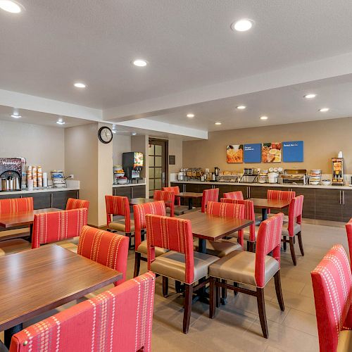 The image shows a brightly lit dining area with red chairs, wooden tables, and a food counter in the background.