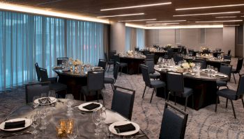 The image shows an elegantly set banquet hall with round tables, black chairs, and formal table settings featuring napkins, plates, and glassware.