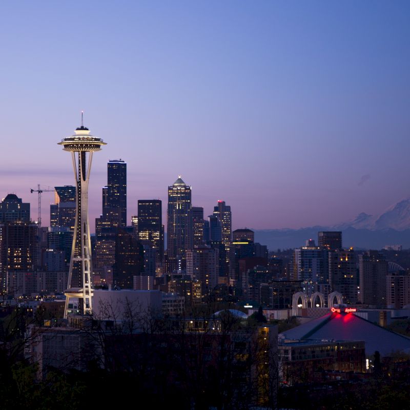 This image shows the Seattle skyline at dusk, featuring the Space Needle prominently, with Mount Rainier visible in the background.
