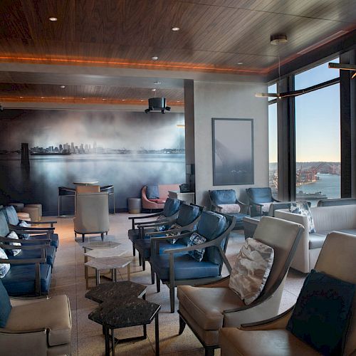 A modern lounge with ample seating, large windows showcasing a cityscape and waterfront view, and stylish decor, perfect for relaxation.