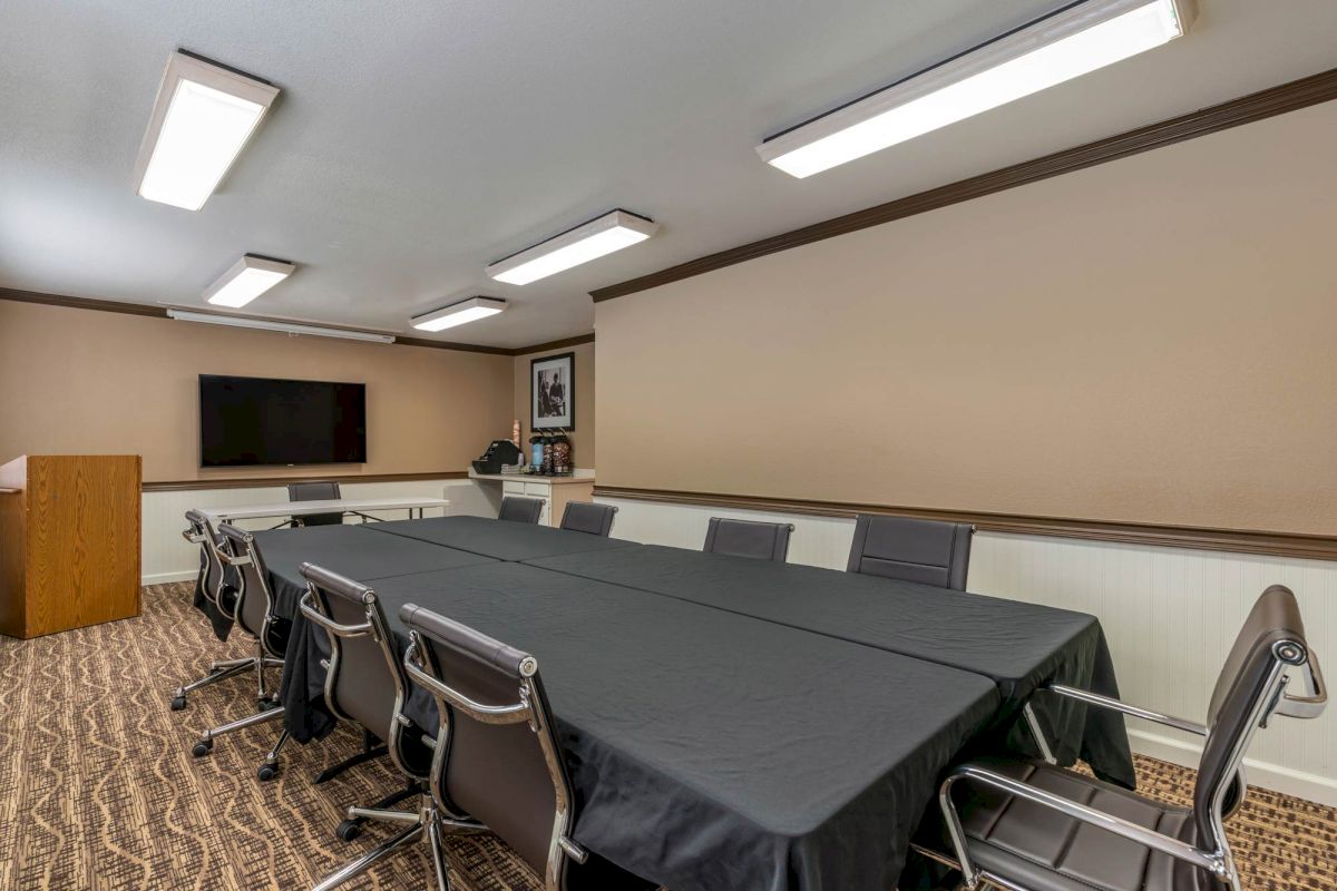 A conference room equipped with a long table, several chairs, a wall-mounted TV, and a podium.