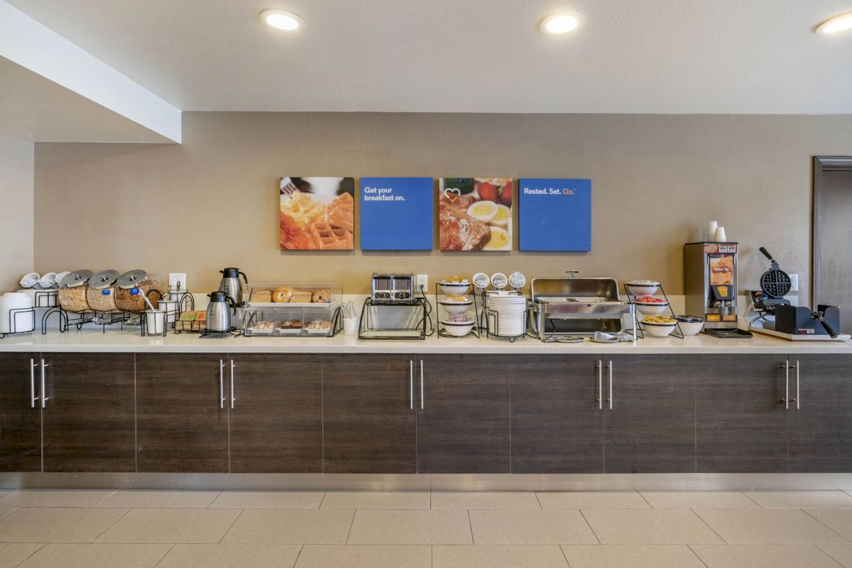 The image shows a breakfast buffet setup with various food and beverage stations, including toasters, coffee dispensers, and waffle makers.